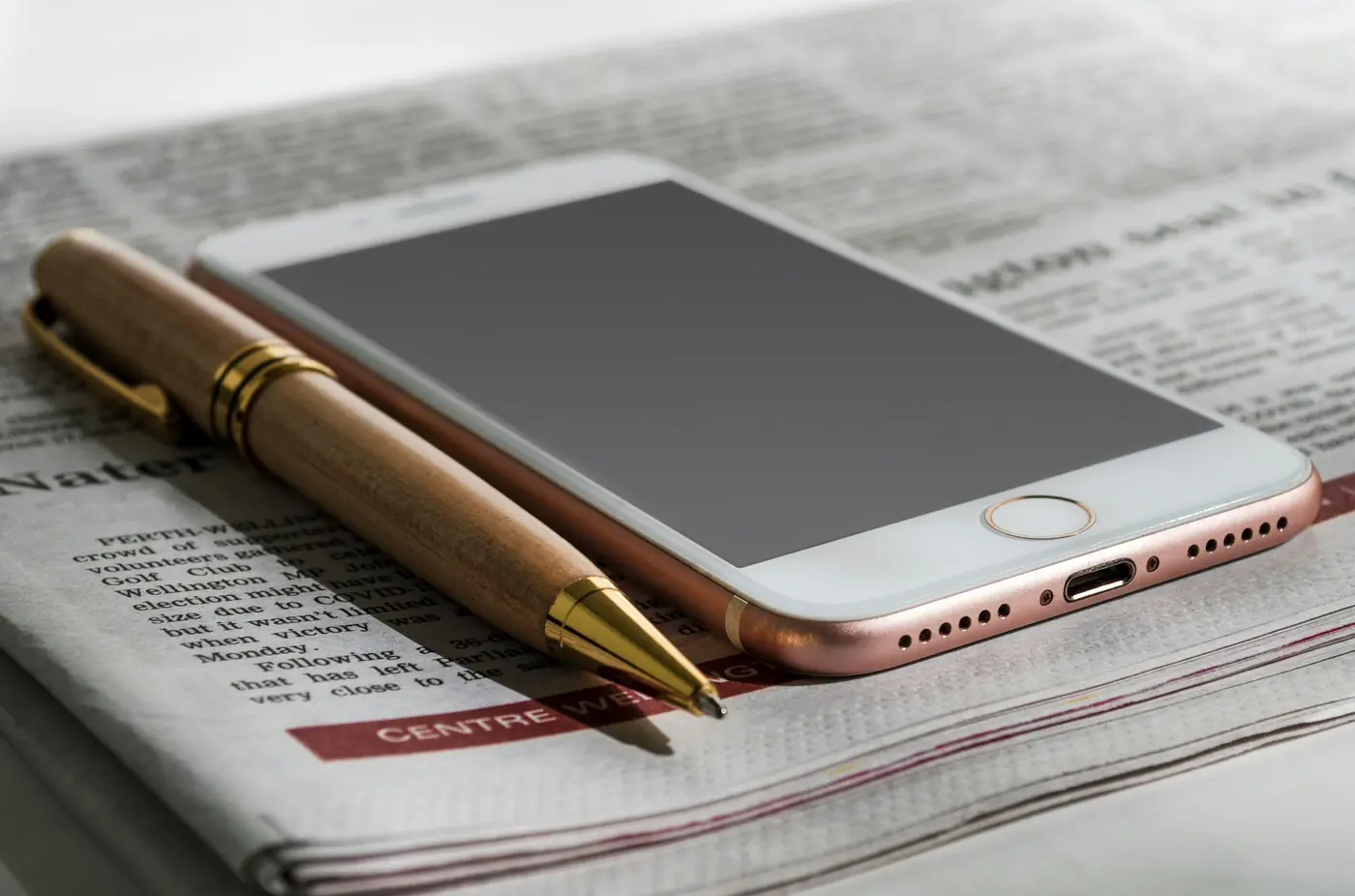 A smartphone and a pen lying on an open newspaper